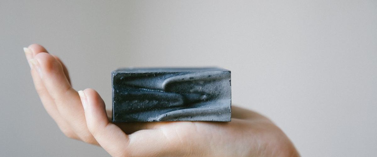 Man holding a dark charcoal soap bar